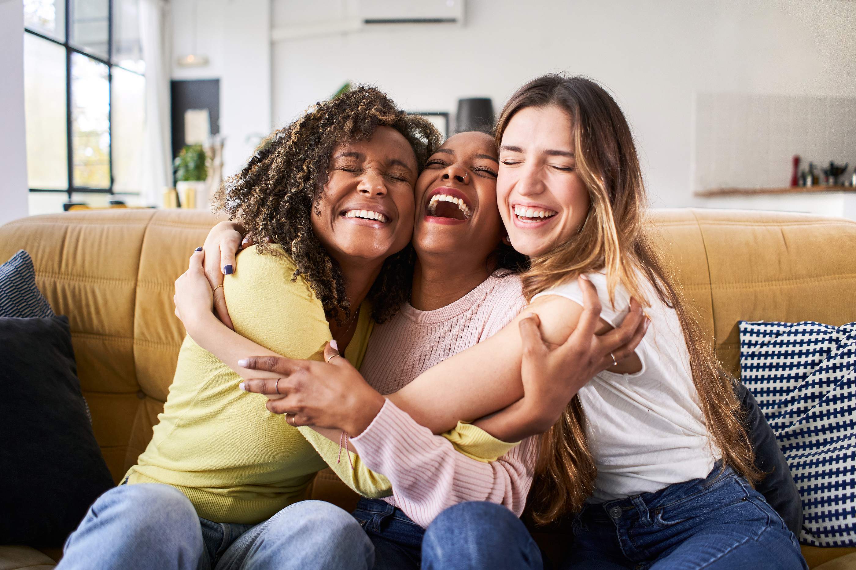 un abrazo en grupo de 3 mujeres sentadas en un sofá sonriendo