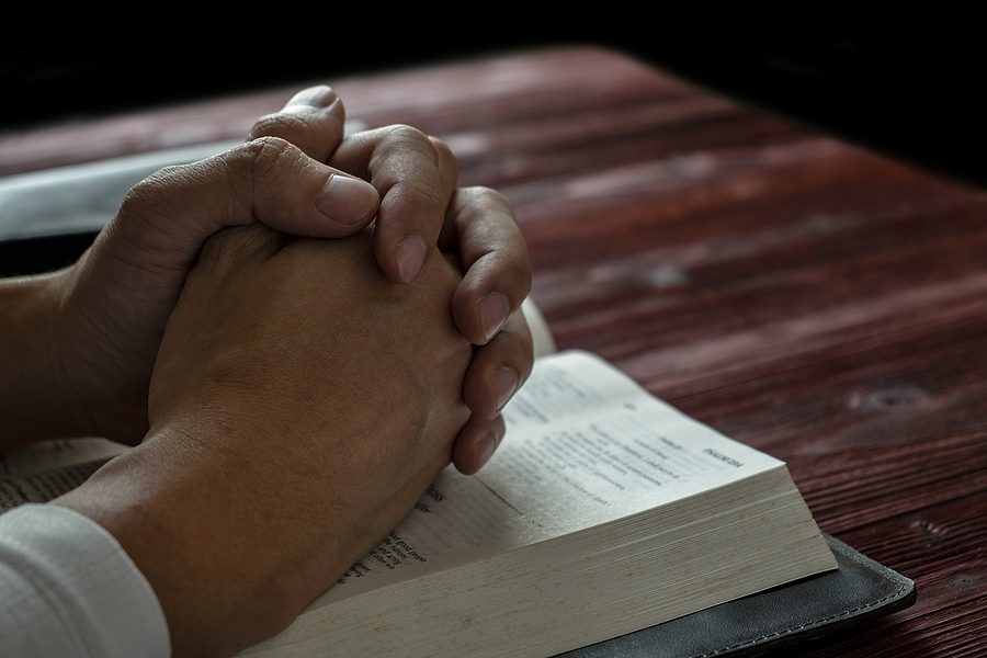 manos cruzadas y descansando sobre una Biblia abierta